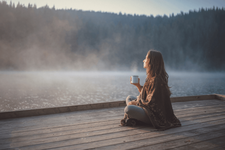 lady sitting next to a river drinking tea - Calm setting for self-reflection after illness